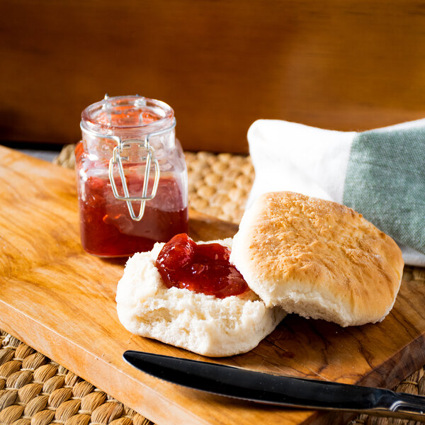 A Bridgford Old South buttermilk biscuit with jam on a wooden cutting board with a knife.