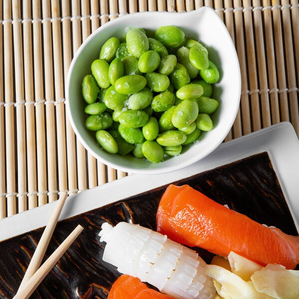 A bowl of shelled soy edamame next to a plate of food with chopsticks.