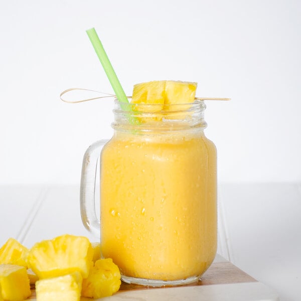 A glass jar with a straw filled with yellow liquid and yellow diced pineapple.
