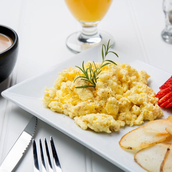 A plate of scrambled eggs and vegetables with a fork and knife on the side.