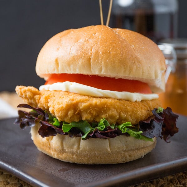 A plate with a chicken burger made with Brakebush Tender-Licious breaded chicken breast fillet, lettuce, and tomato.