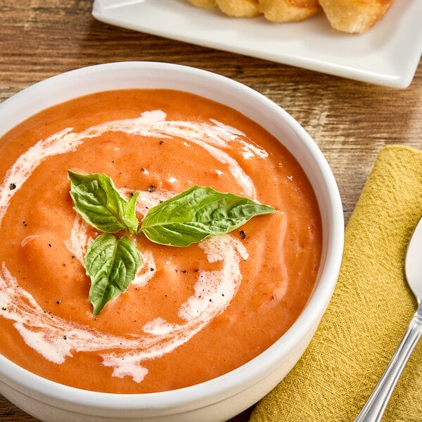 A bowl of Chef Francisco tomato bisque soup with basil leaves on top.