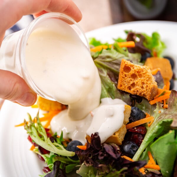A person pouring Ken's Foods Deluxe Bleu Cheese dressing on a salad with vegetables.