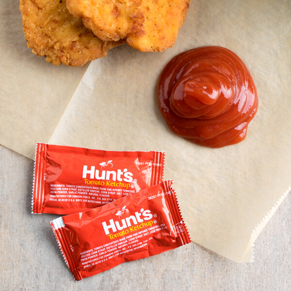 A close up of a chicken nugget next to Hunts Tomato Ketchup packets.