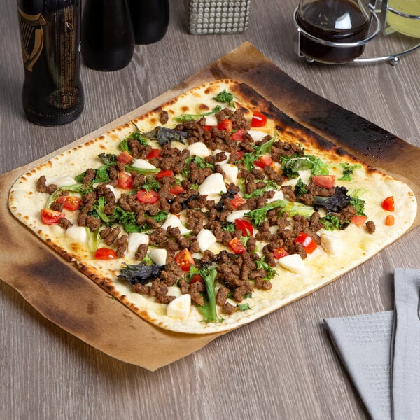 A Rich's oven fired flatbread with meat and vegetables on a wooden table.