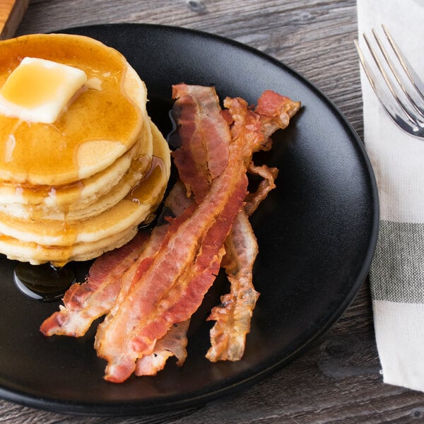 A black plate with a stack of pancakes, butter, and Hormel Fast 'N Easy bacon slices.