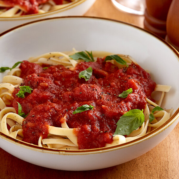 A bowl of Angela Mia spaghetti with sauce and basil leaves.