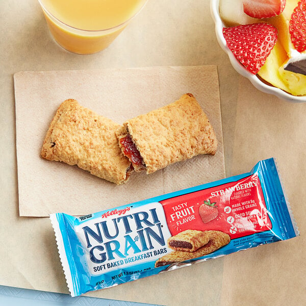 A Kellogg's Nutri Grain strawberry cereal bar on a breakfast bar with a bowl of fruit and a glass of juice.