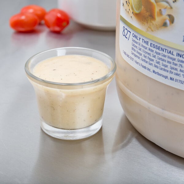 A jar of Ken's Creamy Caesar dressing next to a small glass of white liquid.