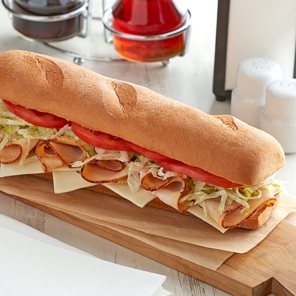 A Udi's gluten-free hoagie roll sandwich with meat and vegetables on a table.
