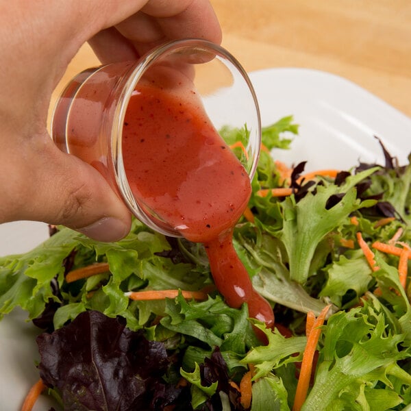 A hand pouring Ken's Lite Raspberry Vinaigrette over a vegetable salad.