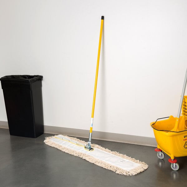 A Lavex all-in-one cotton dust mop with a handle on the floor next to a trash can.