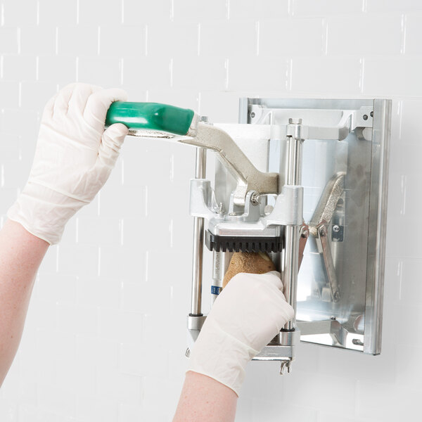 A person wearing white gloves using a Garde French fry cutter with a wall mount bracket.