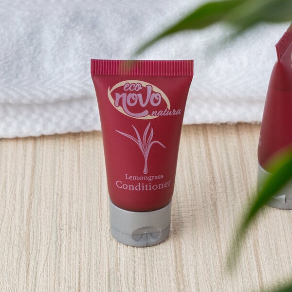 A small red tube of Noble Eco Novo Natura conditioner with white text next to a white towel.