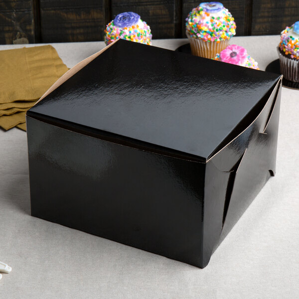 A black Enjay bakery box with a lid and a cupcake on a table.