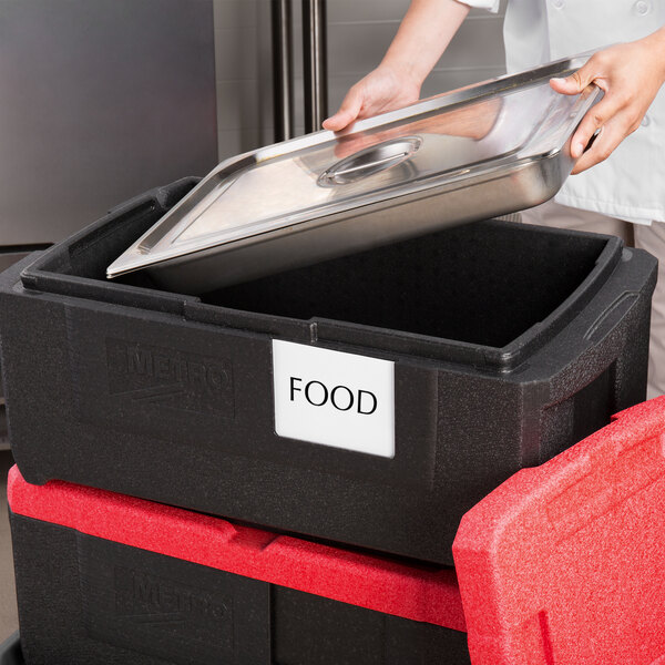 A person putting a tray of food into a black Metro Mightylite food pan carrier.