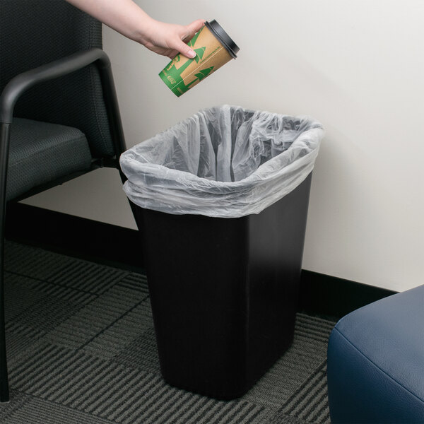 A hand throwing a coffee cup into a black rectangular Continental trash can.