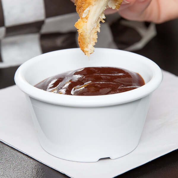 A person using a fork to dip a piece of fried chicken in white ramekin of sauce.