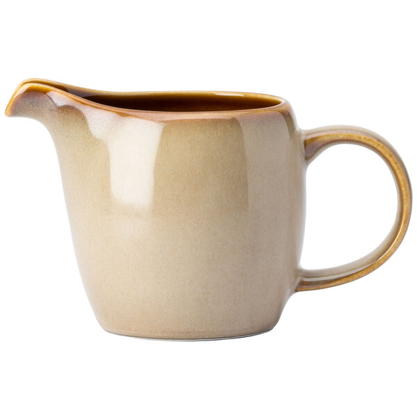 A cream colored ceramic pitcher with a brown handle.