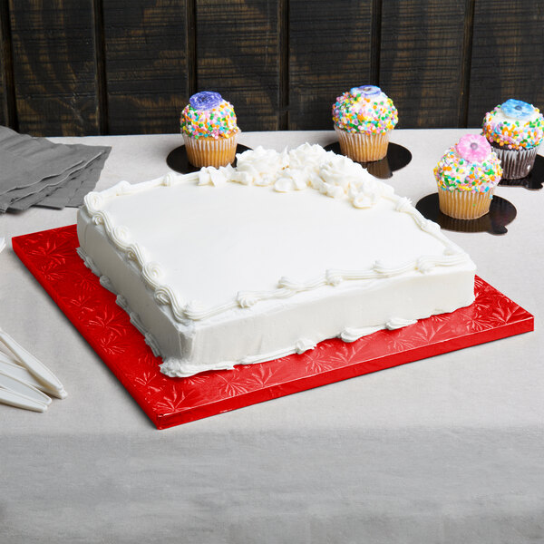 A white frosted cake on a red Enjay square cake drum with sprinkles on top.