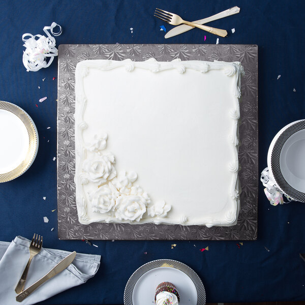 A white square cake on an Enjay black square cake drum with silverware.