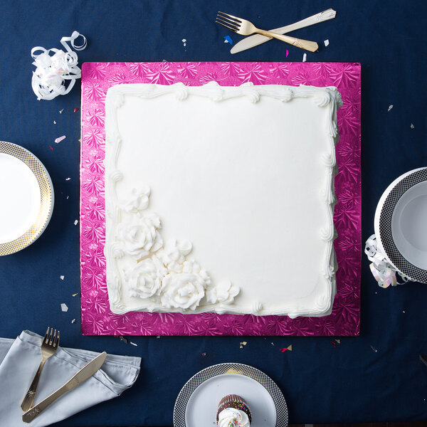 A white square cake on a pink cake drum on a white plate with a black and white checkered pattern.