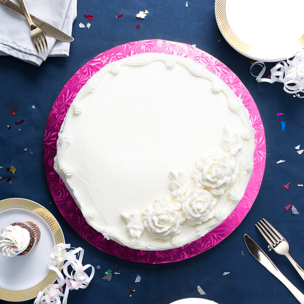 A white cake with white frosting on a pink Enjay cake drum with silverware.