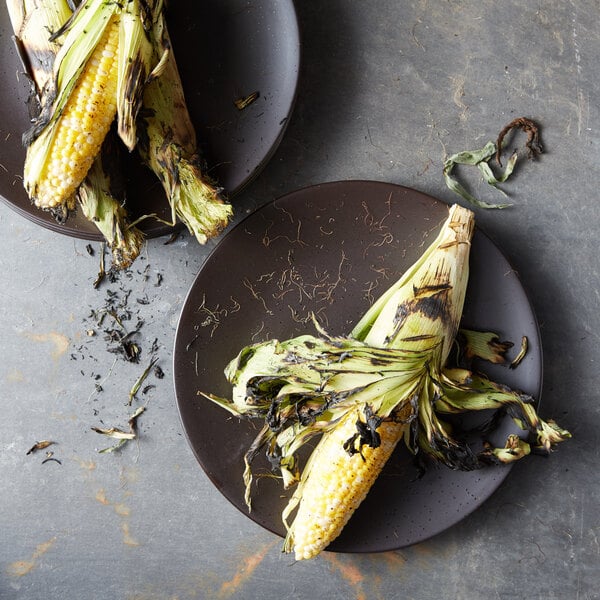 Two Oneida Lava porcelain plates with grilled corn on them.