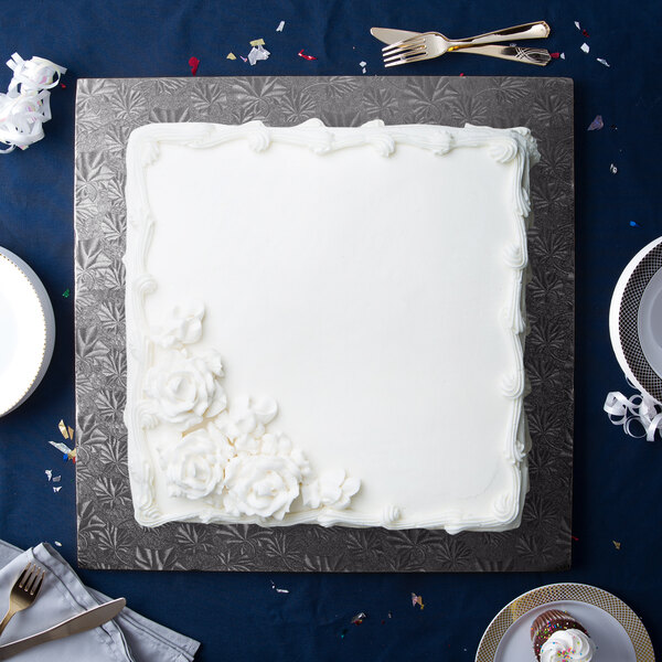 A white square cake on a black Enjay cake board with white flowers on top.