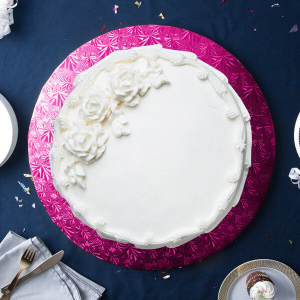 A white cake with white frosting and flowers on a pink Enjay round cake board.