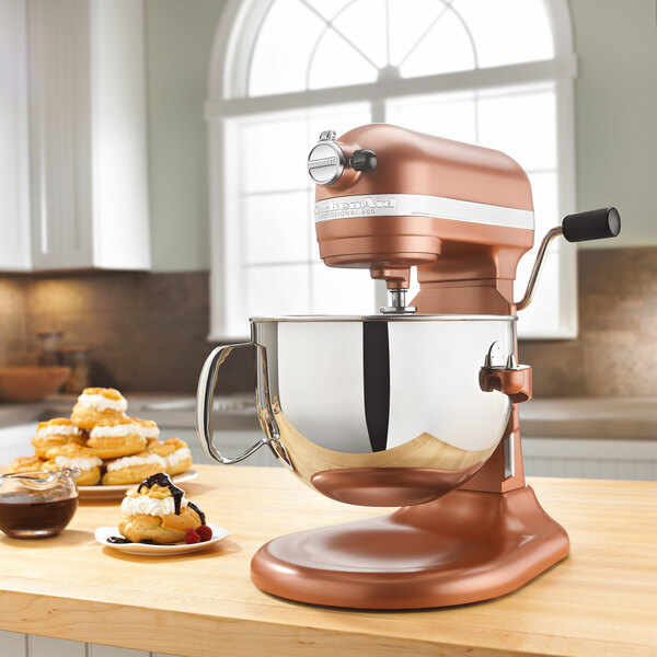 A KitchenAid copper pearl countertop mixer with a bowl of brown batter sitting on the counter.