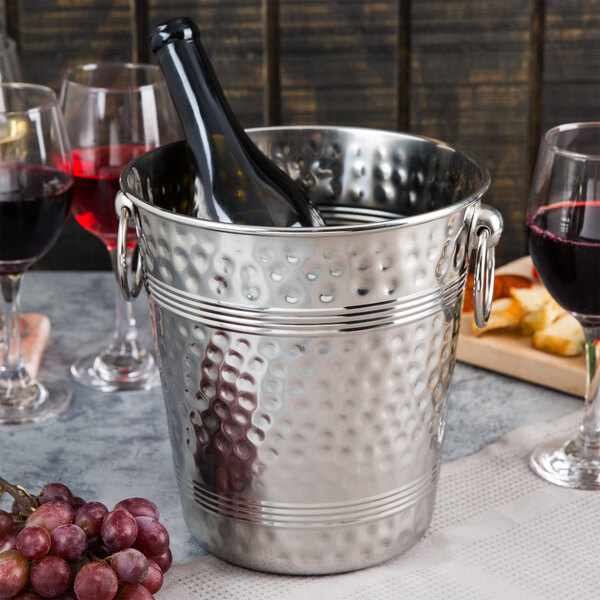 A Tablecraft stainless steel wine bucket with a bottle of wine and two glasses inside.