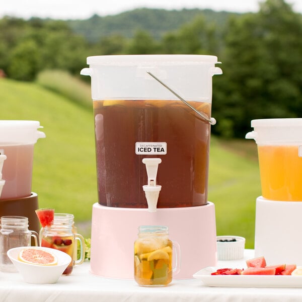 A Choice translucent beverage dispenser with a drink and lemon slices on a table with tea and fruit.