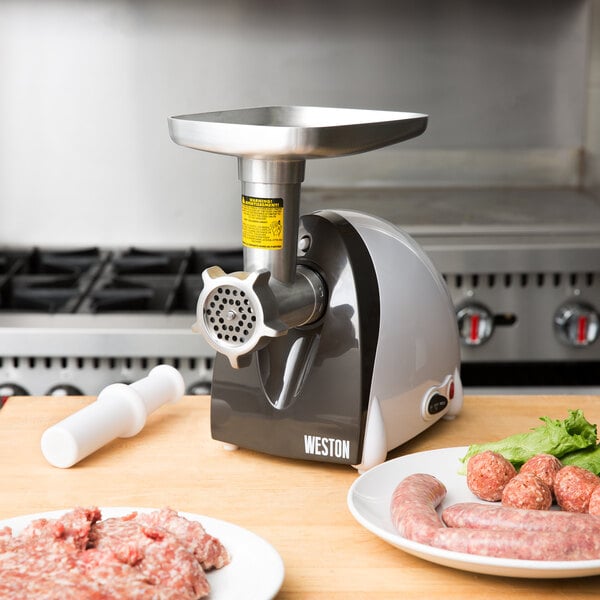 A silver Weston Electric Meat Grinder on a table with meat and vegetables.