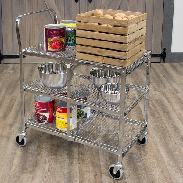 A Luxor metal utility cart with wire shelves holding food containers and a crate on top.