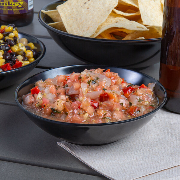 A black melamine bowl of salsa with tomatoes and onions on a table.