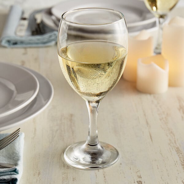 An Anchor Hocking Excellency white wine glass filled with white wine on a table.