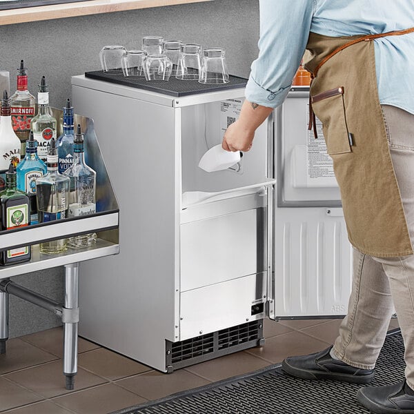 A man standing next to a Hoshizaki undercounter ice machine on a counter in a cocktail bar.