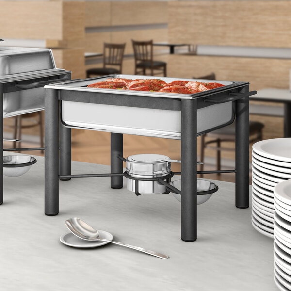 An Acopa wrought iron chafer with a stainless steel cover on a buffet table with plates and bowls.
