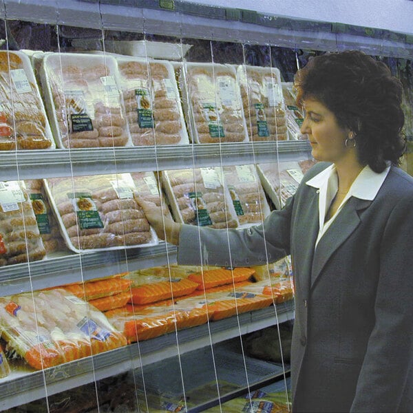 A woman looking at a display of meats through a Curtron display cooler strip curtain.