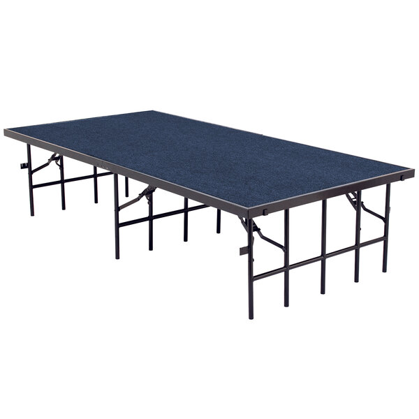 A National Public Seating single height portable stage with blue carpet on a rectangular table with black legs.