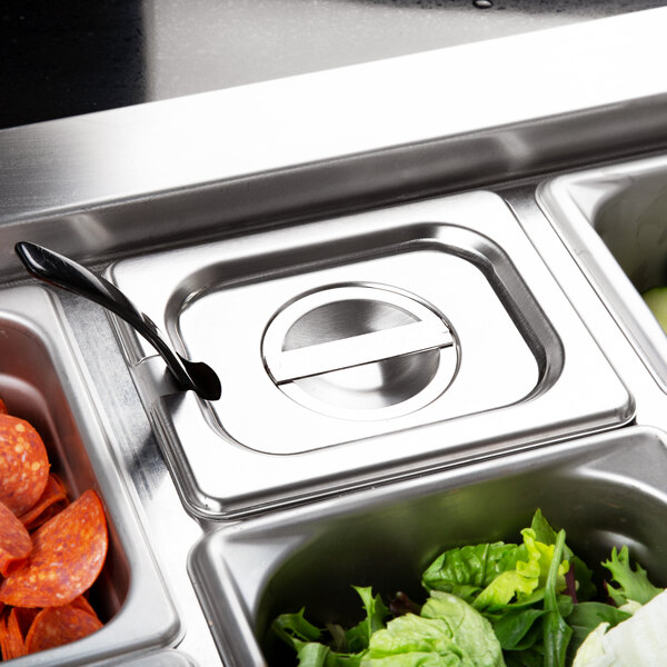 A Vollrath stainless steel slotted hotel pan cover on a counter with a tray of food.