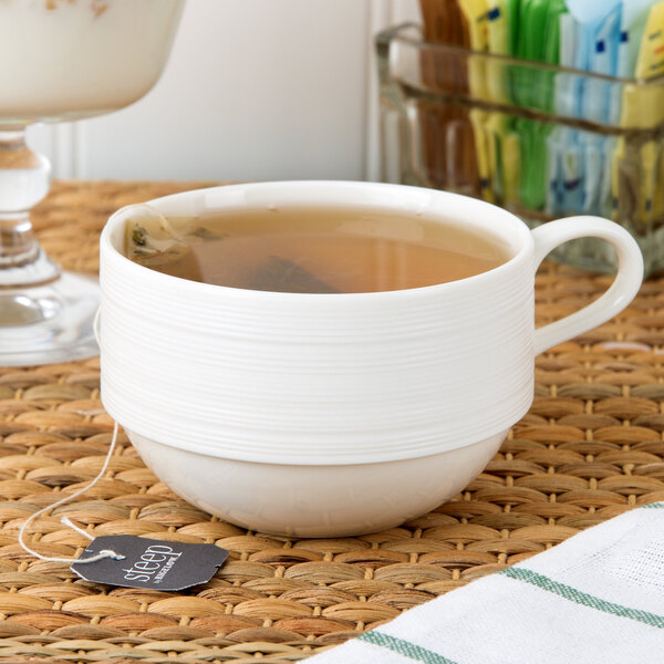 A Oneida warm white porcelain cup filled with tea on a saucer.