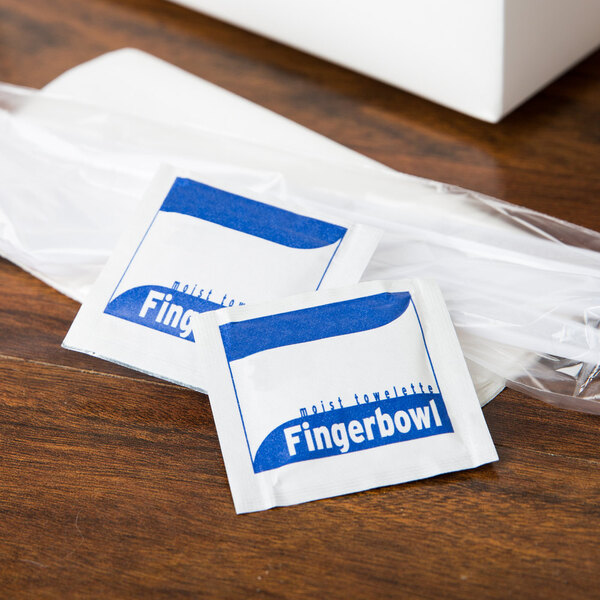 A wooden surface with white and blue Royal Paper Lemon Scented Hand Wipe packets.