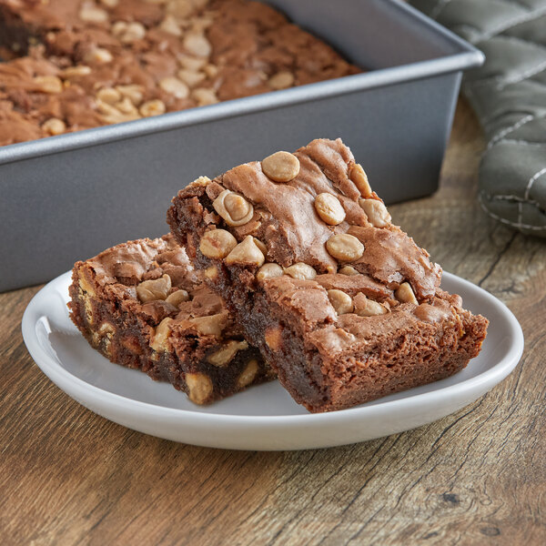 A white plate of brownies with nuts on top.