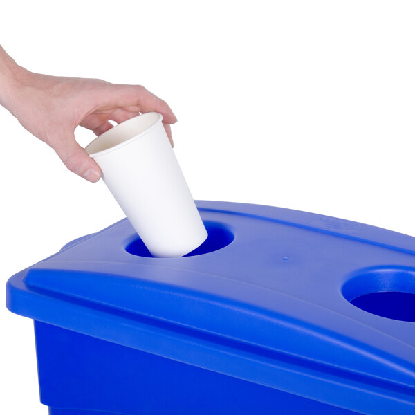 A hand putting a white cup into a blue rectangular wall hugger recycle container with a white lid.