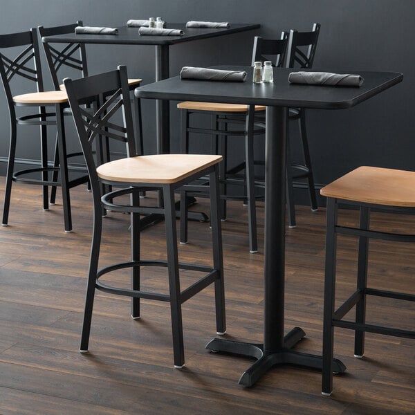 A Lancaster Table & Seating black cross back bar stool with a natural wood seat on a table in a restaurant.