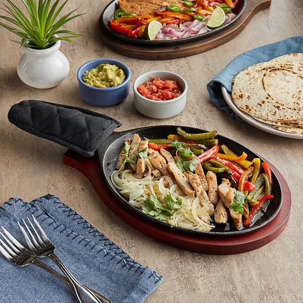 A Choice oval cast iron fajita skillet with food on it and a bowl of red sauce on a table.