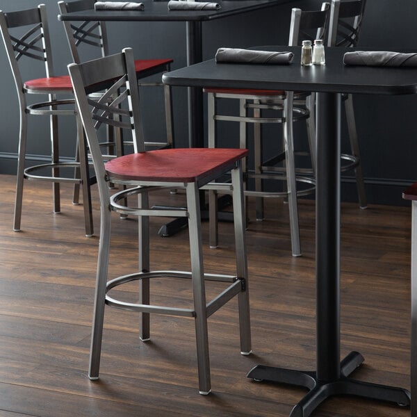 A Lancaster Table & Seating bar stool with a mahogany seat on a table with a napkin and salt shakers.