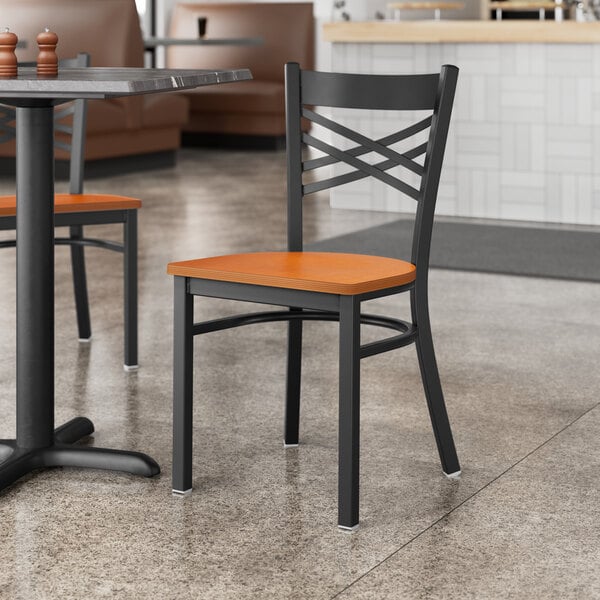 A Lancaster Table & Seating black cross back chair with a cherry wood seat at a table in a restaurant.